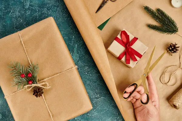 Vue recadrée de la femme avec des ciseaux près des boîtes cadeaux fournitures de décoration de Noël sur texture bleue — Photo de stock