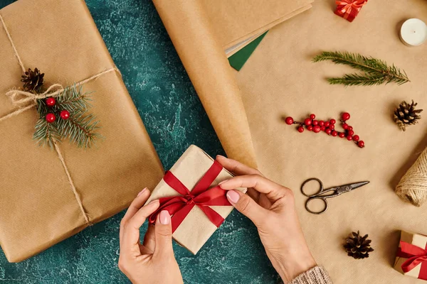 Vue recadrée de la femme attachant arc rouge sur boîte cadeau tout en faisant cadeau de Noël près de fournitures de décoration — Photo de stock