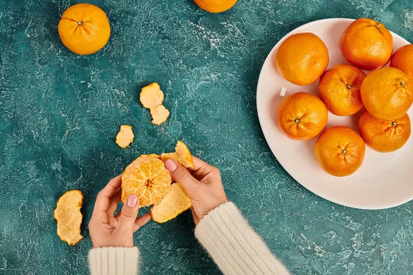 Partial view of woman peeling fresh ripe mandarin on blue textured surface, Christmas concept — Stock Photo