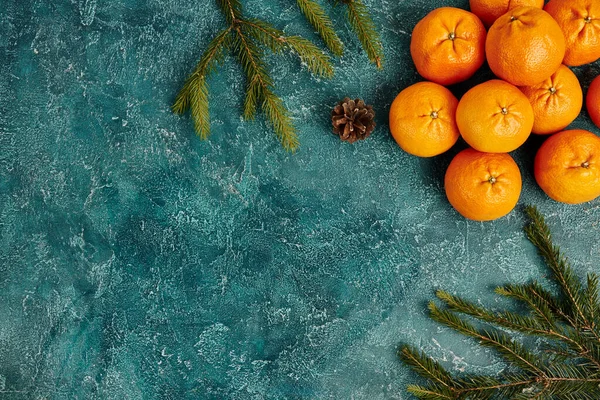 Reife Mandarinen und Tannenzweige mit Tannenzapfen auf blau strukturiertem Hintergrund mit Kopierraum — Stockfoto