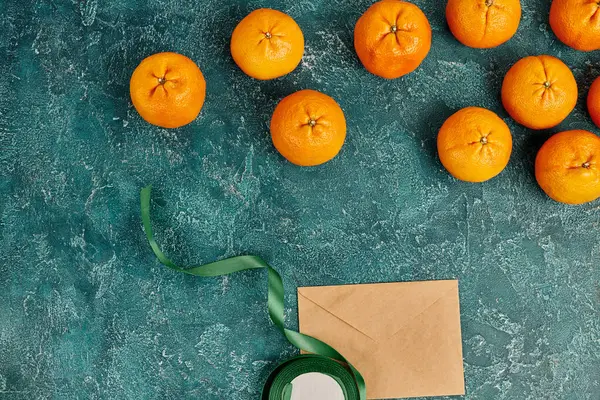 Bodegón de Navidad con mandarinas maduras y sobre de poste cerca de cinta decorativa en superficie azul - foto de stock