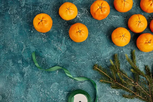 Fresh mandarins next to pine branch and decorative ribbon on blue textured backdrop, Christmas — Stock Photo