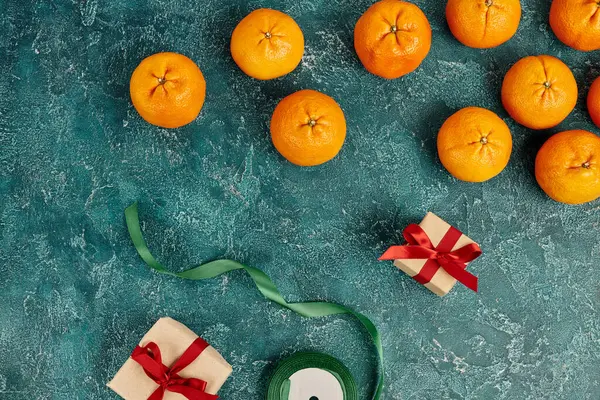 Decorated gift boxes near fresh mandarins and ribbon on blue textured surface, Christmas still life — Stock Photo