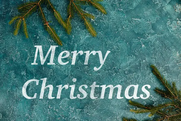 Feliz Natal saudação na superfície rústica azul perto de ramos de pinho verde, fundo festivo — Fotografia de Stock