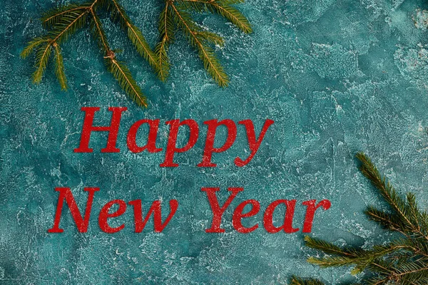 Feliz ano novo inscrição na superfície texturizada azul perto de ramos de pinho verde, fundo festivo — Fotografia de Stock