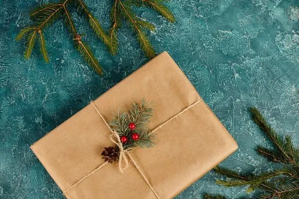 Geschenkschachtel aus Bastelpapier, dekoriert mit Stechpalmen in der Nähe von Kiefernzweigen auf blauem Hintergrund, Weihnachten — Stockfoto