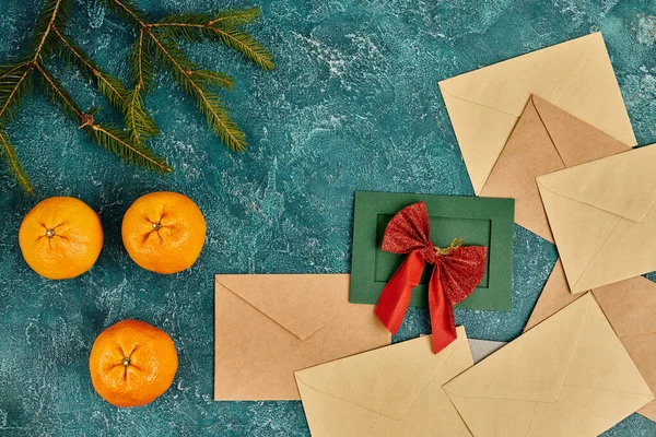 Green card with red bow near envelopes, tangerines and pine branches on blue backdrop, Christmas — Stock Photo