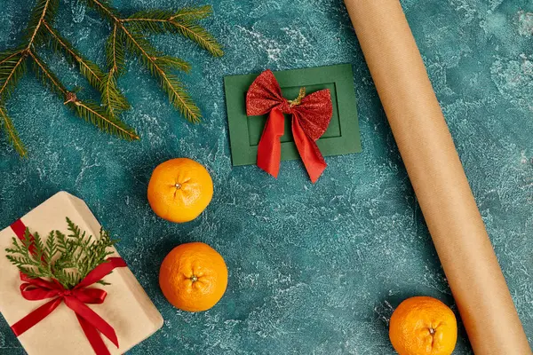 Tarjeta de felicitación hecha a mano cerca del rollo de papel artesanal en la superficie de textura azul con caja de regalo y mandarinas - foto de stock