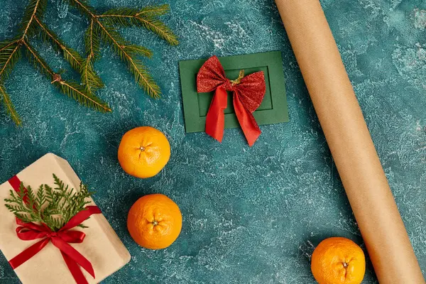 Cartão de saudação artesanal perto do rolo de papel artesanal na superfície texturizada azul com caixa de presente e tangerinas — Fotografia de Stock