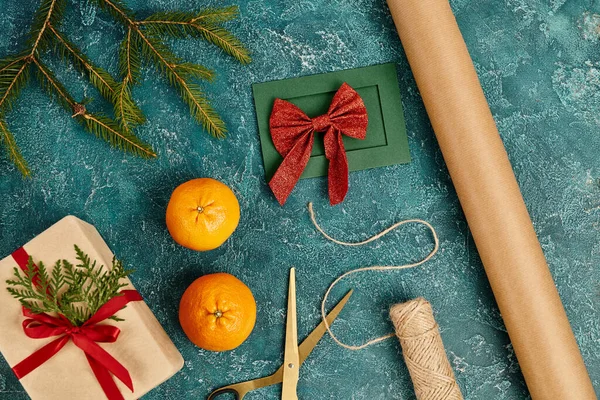 Fournitures de décoration près de la main carte de vœux et boîte cadeau sur la surface bleue avec des branches de pin, bricolage — Photo de stock