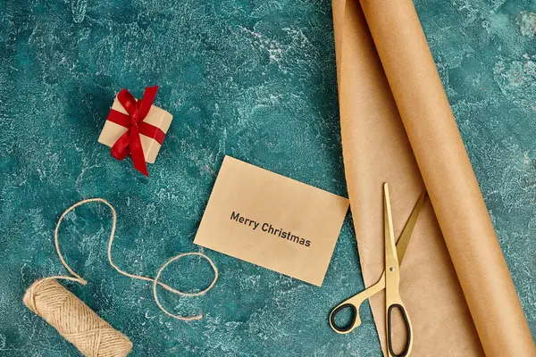 Envelope com Feliz Natal saudação perto de caixa de presente e materiais de decoração em azul, artesanato de férias — Fotografia de Stock