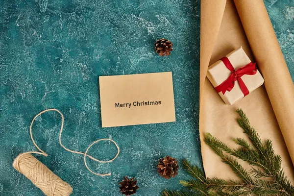 Envelope com Feliz Natal saudação perto de decoração de pinho e suprimentos diy em fundo azul texturizado — Fotografia de Stock
