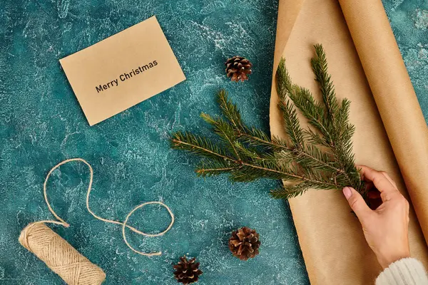 Vue recadrée de la femme avec branche de pin près de l'enveloppe avec Joyeux Noël lettrage et fournitures bricolage — Photo de stock