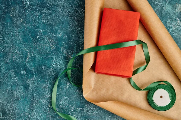 Boîte cadeau rouge et papier artisanal avec ruban décoratif sur fond texturé bleu, cadeau de Noël bricolage — Photo de stock