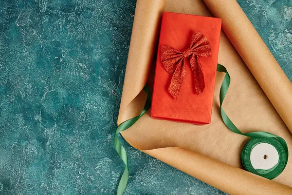 Boîte cadeau avec ruban rouge sur papier artisanal près du ruban décoratif sur fond texturé bleu, Noël — Photo de stock