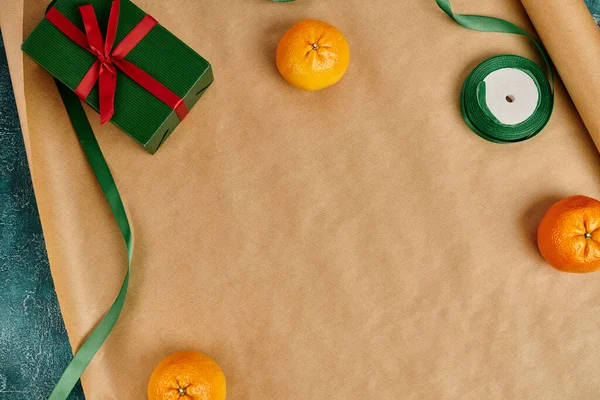 Верхний вид спелых мандаринов и зеленая подарочная коробка с красным луком и декоративной лентой на бумаге — стоковое фото