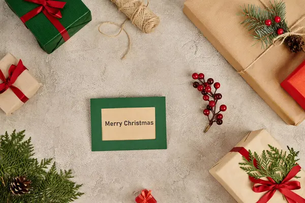 Feliz Natal cartão perto de caixas de presente e decoração festiva de Natal na superfície texturizada cinza — Fotografia de Stock