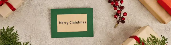 Cartão de saudação com letras Feliz Natal perto de caixas de presente e bagas de azevinho, bandeira horizontal — Fotografia de Stock