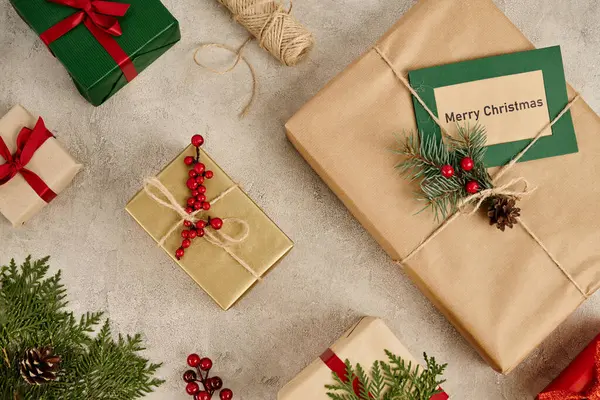 Telón de fondo festivo, tarjeta de felicitación Feliz Navidad cerca de cajas de regalo con ramas de pino y bayas de acebo - foto de stock