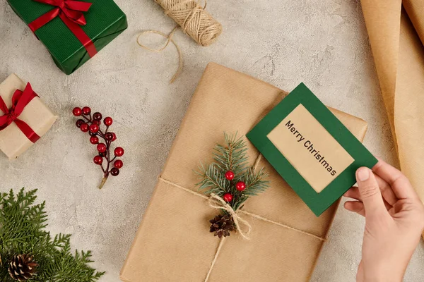 Geschenkbox mit Frohe Weihnachten Grußkarte in der Nähe von Geschenken und saisonalem Dekor auf strukturierter Oberfläche — Stockfoto
