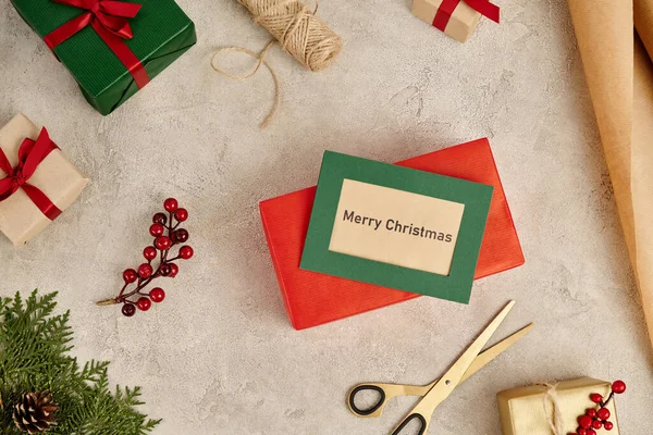 Tarjeta de felicitación de Feliz Navidad cerca de cajas de regalo multicolores y ramas de enebro con bayas de acebo - foto de stock