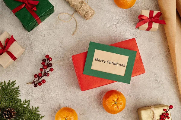 Tarjeta de felicitación de Feliz Navidad cerca de mandarinas y cajas de regalo decoradas sobre fondo texturizado gris - foto de stock