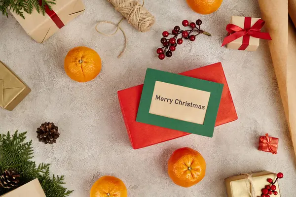 Tarjeta de felicitación de Feliz Navidad cerca de mandarines y regalos decorados sobre fondo texturizado gris - foto de stock