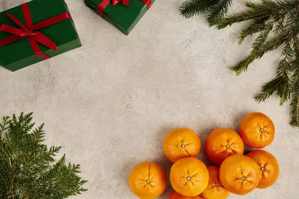 Marco con mandarinas maduras y cajas de regalo verdes cerca de ramas de enebro y pino en superficie texturizada - foto de stock