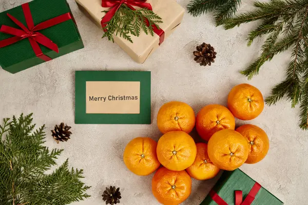 Mandarines et Joyeux Noël carte de voeux près de boîtes-cadeaux et décor festif avec des branches de pin — Photo de stock