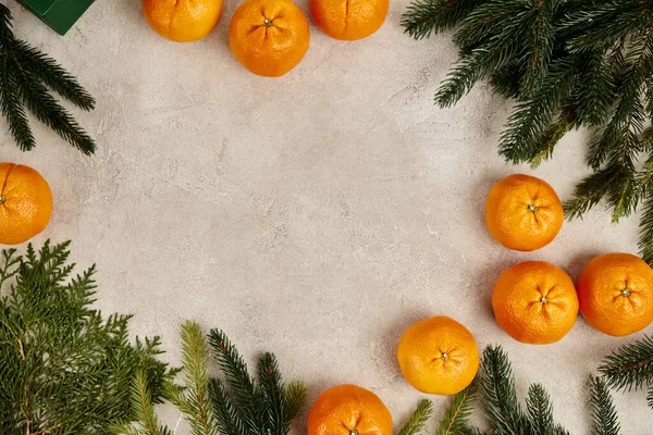 Weihnachtsrahmen mit süßen Mandarinen in der Nähe von Wacholder und Kiefernzweigen auf grau strukturierter Oberfläche — Stockfoto