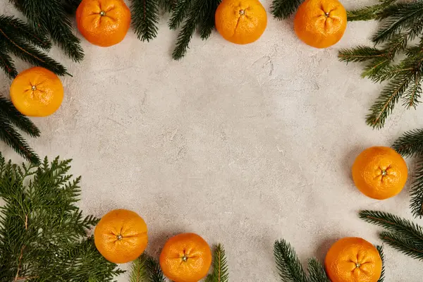 Weihnachtsrahmen mit reifen Mandarinen in der Nähe von Wacholder- und Kiefernzweigen auf grau strukturiertem Hintergrund — Stockfoto