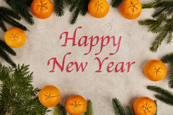 Happy new year lettering in frame of tangerines with pine and juniper branches on grey texture — Stock Photo