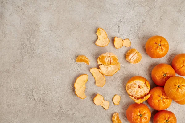 Vista superior de mandarinas maduras inteiras e descascadas em pano de fundo texturizado cinza, conceito de Natal — Fotografia de Stock