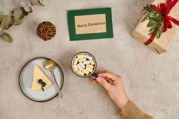 Mulher com caneca de chocolate quente com marshmallows perto de pudim e cartão de felicitações Feliz Natal — Fotografia de Stock