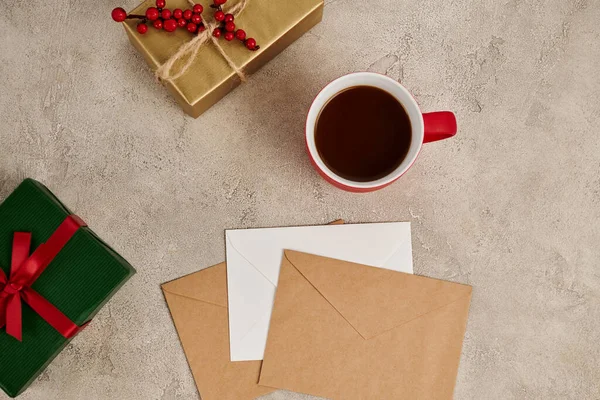 Chocolate quente perto de caixas de presente multicoloridas e envelopes em fundo de Natal texturizado cinza — Fotografia de Stock