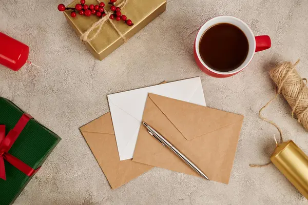 Chocolat chaud près des enveloppes et boîtes cadeaux avec des bougies sur fond gris texturé, Noël — Photo de stock