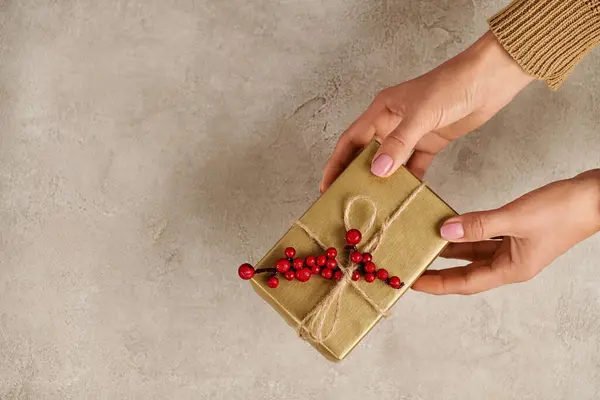Vista ritagliata della donna con scatola regalo dorata decorata con bacche di agrifoglio, allegria natalizia — Foto stock
