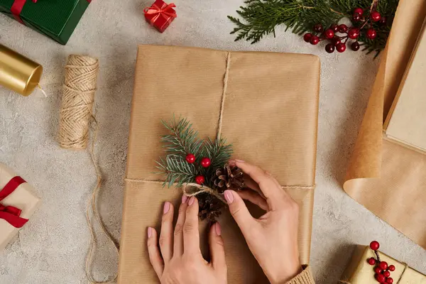 Vista cortada de mulher decorando presente de Natal com cones de abeto e ramos de pinho com bagas azevinho — Fotografia de Stock