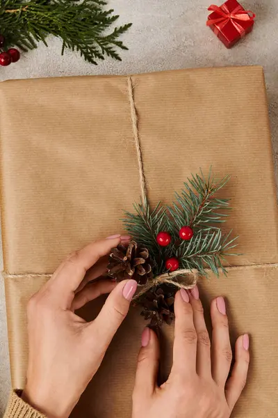 Femme cultivée décorant boîte cadeau avec cônes de sapin et branches de pin avec des baies de houx, Noël — Photo de stock