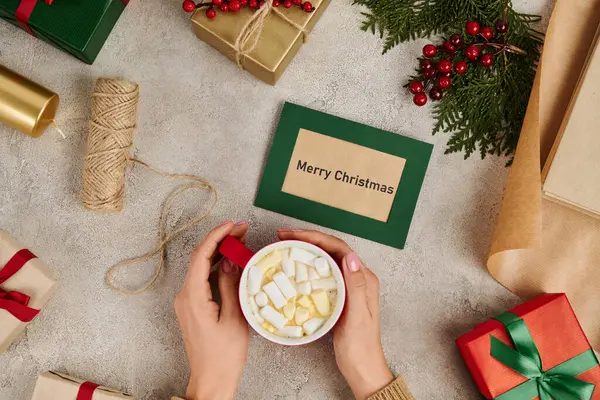 Cropped view of woman holding hot chocolate with marshmallows near Merry Christmas greeting card — Stock Photo