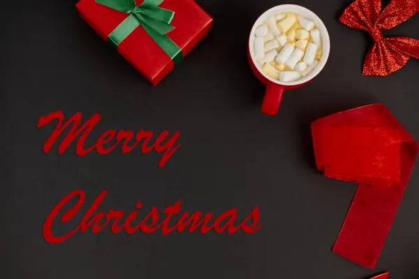 Rosso Buon Natale lettering vicino confezione regalo e fiocco lucido con nastro su sfondo nero, tema festa — Foto stock