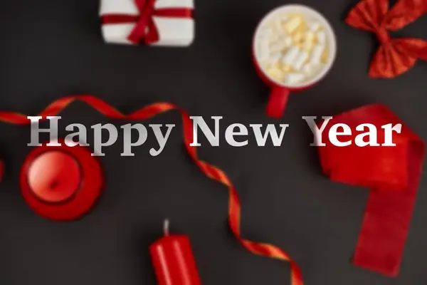 Happy new year lettering over blurred Christmas background with red festive decor on black surface — Stock Photo