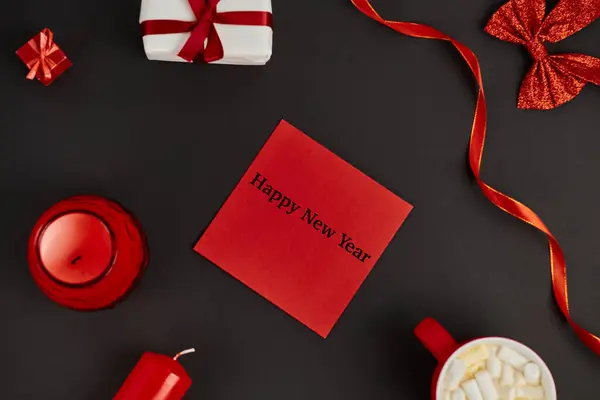 Red envelope with happy new year greeting near hot chocolate with marshmallows and decor on black — Stock Photo