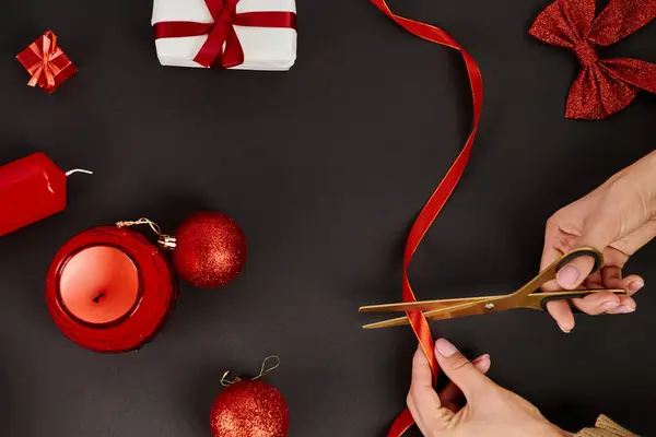 Vue recadrée du ruban de coupe femme avec ciseaux près des boules et décor de Noël sur noir — Photo de stock