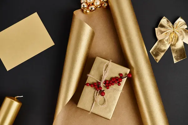 Decoração de Natal dourada, caixa de presente com bagas de azevinho em papel de embrulho perto de vela e arco em preto — Fotografia de Stock