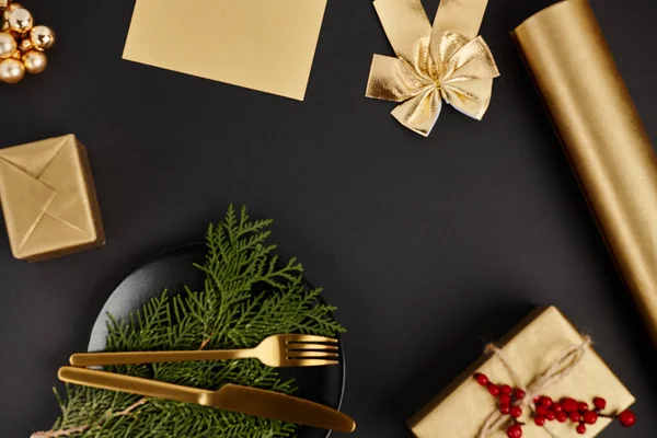 Posate dorate su rami di ginepro vicino a decorazioni natalizie lucenti su sfondo nero, esclusività — Foto stock