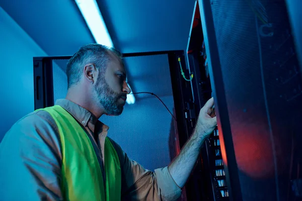 Good looking bearded specialist in safety clothes working attentively and inspecting data center — Stock Photo