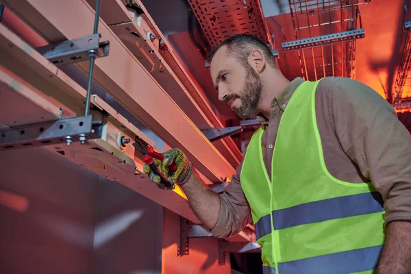 Handsome focused professional in safety vest and gloves using pliers while working hard, data center — Stock Photo