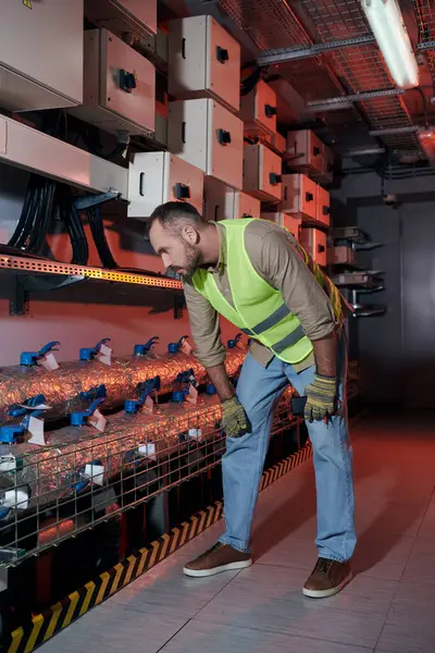 Attractive concentrated technician in safety gloves and vest leaning while working in data center — Stock Photo