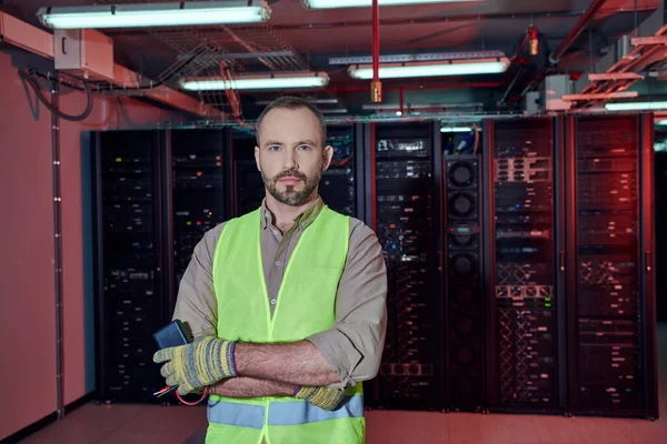 Good looking technician in safety vest and gloves posing with arms crossed on chest, data center — Stock Photo